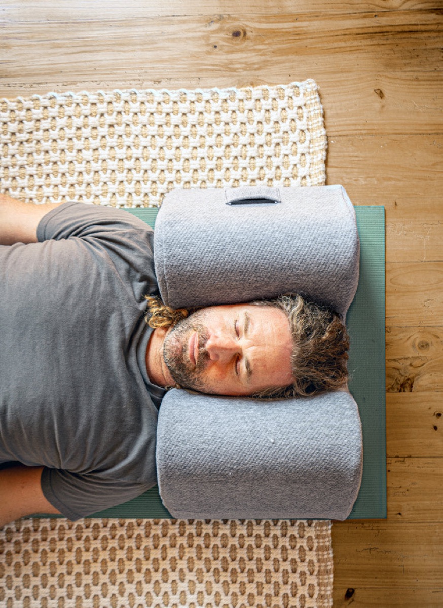 Whit Hansen, founder of Drop Pillow, lying on a wooden floor with his head resting in the pillow
