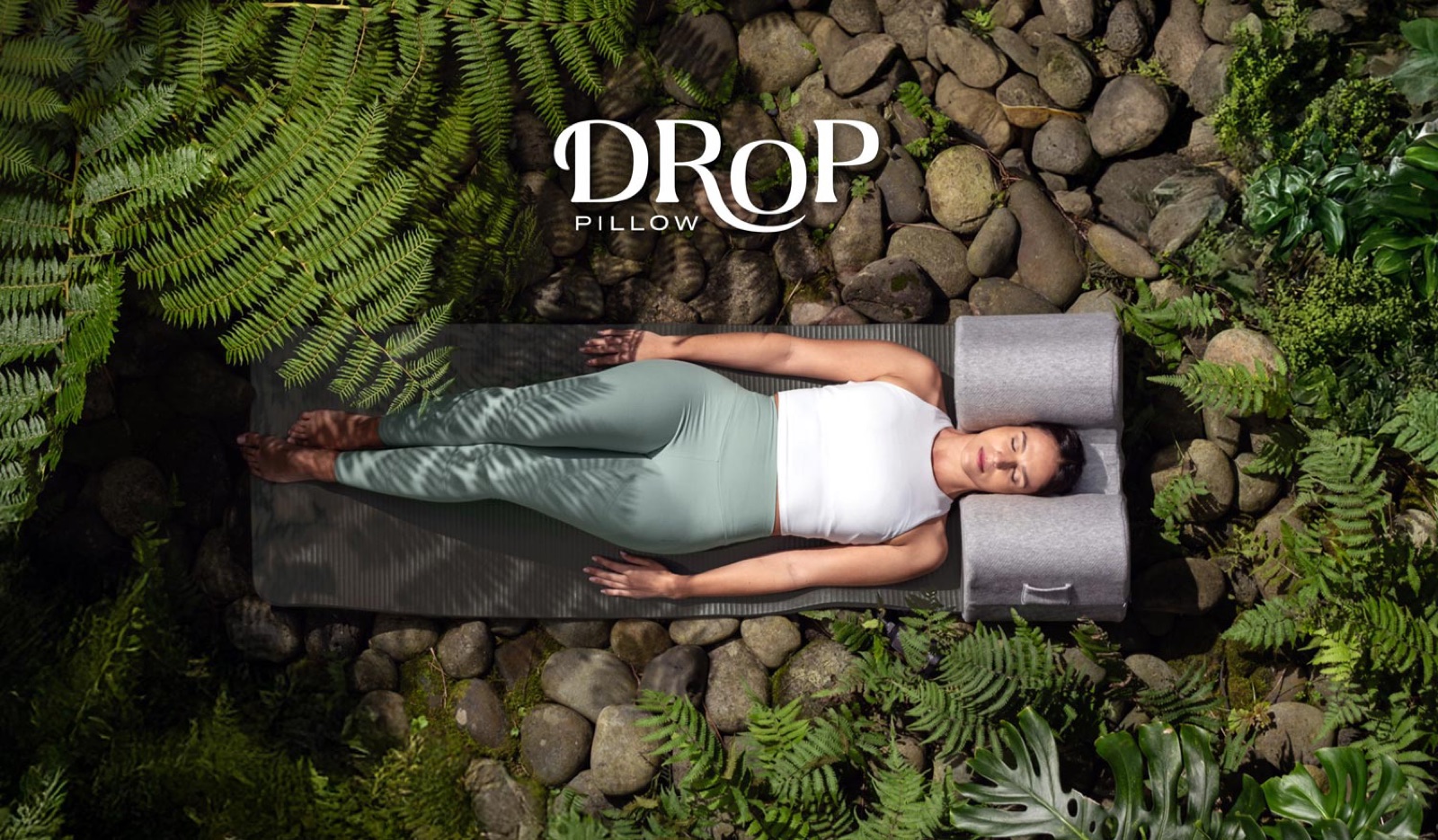 Seen from above: a woman lying on a mat among ferns with her head between the pillow’s arms