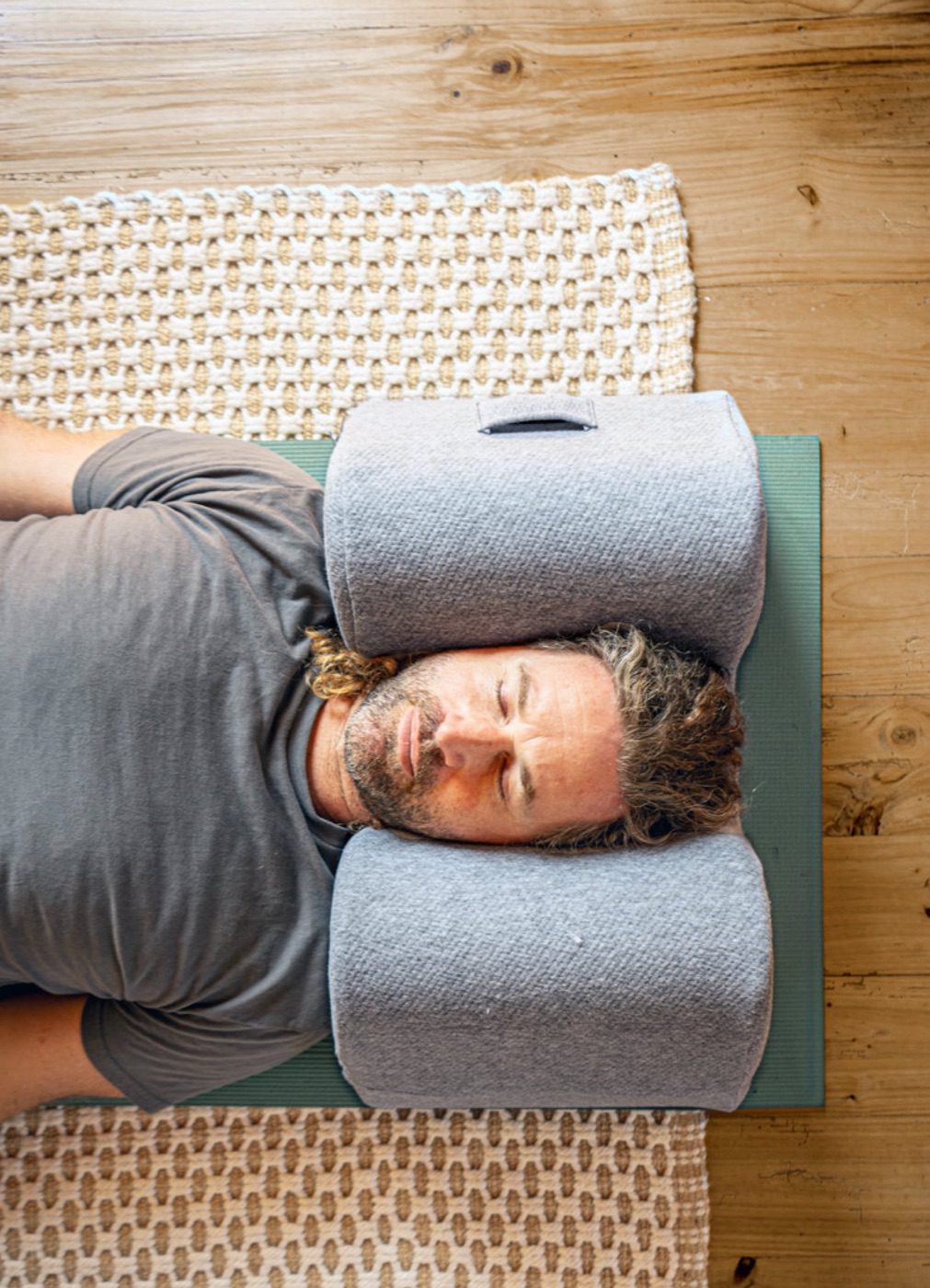 A man lying on a wooden floor with his head resting in the pillow, eyes closed