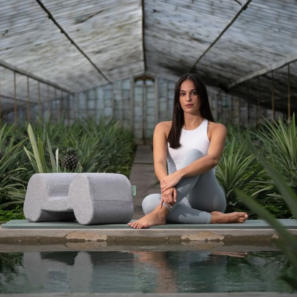 The Drop Pillow on a mat beside a woman sitting in a greenhouse
